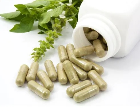Ayurvedic herbal capsules spilling from a bottle alongside fresh basil leaves